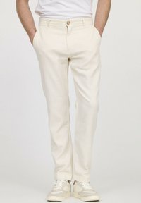 Pantalon crème avec une finition texturée, doté d'une fermeture à bouton, de poches latérales et de jambes fuselées, associé à des baskets légères.