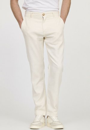 Pantalon crème avec une finition texturée, doté d'une fermeture à bouton, de poches latérales et de jambes fuselées, associé à des baskets légères.