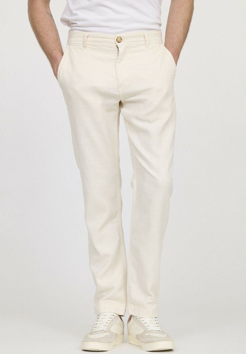 Pantalon crème avec une finition texturée, doté d'une fermeture à bouton, de poches latérales et de jambes fuselées, associé à des baskets légères.