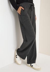 Pantalones grises de tela tejida con un corte relajado, que cuentan con una cinturilla elástica y cordón, bolsillos laterales y se combinan con zapatillas blancas.