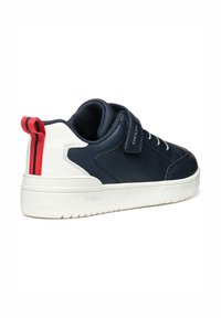 Zapatilla navy y blanca con parte superior de cuero texturizado, bucle en el talón rojo contrastante, cierre de cordones en la parte delantera y laterales perforados para transpirabilidad.