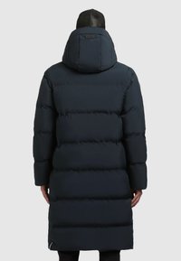 Tumedal puffer-jakk, millel on kapuuts, eriti tikitud disain, pikkus ja elastsed mansetid. Silmapaistev logo seljal ja külgmine tõmblukk.