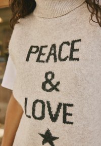 Maglione beige a collo alto in maglia con testo nero che recita "PACE & AMORE" e un design a stella, realizzato in morbido tessuto testurizzato.