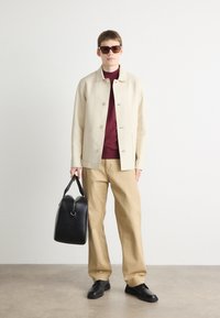 Beige jacket, maroon shirt, beige trousers, black shoes, oversized sunglasses. Black bag with rounded top and handle. Smooth textures.