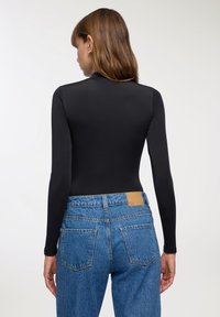 Body a maniche lunghe nero abbinato a jeans in denim blu a vita alta. Le caratteristiche notevoli includono una trama liscia e un'etichetta in pelle color tabacco sui jeans.