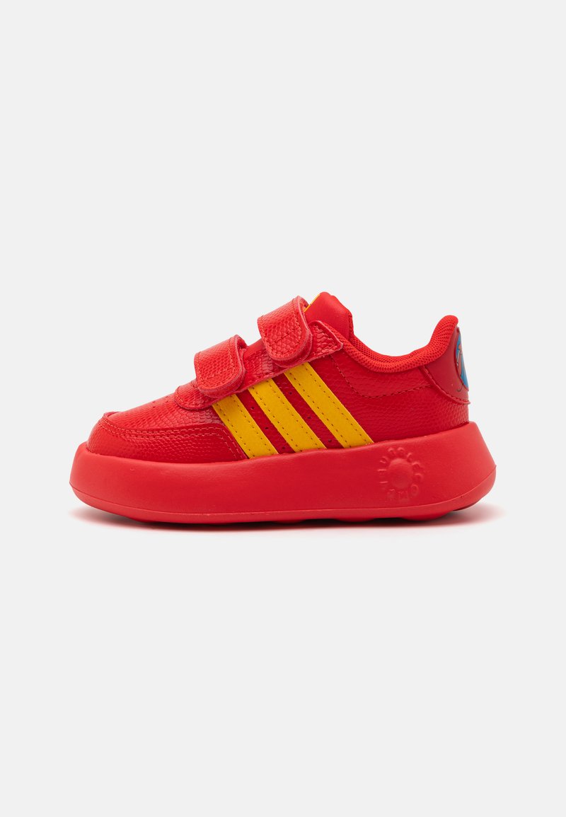 Basket rouge avec une tige texturée, accents de trois bandes jaunes, double bandoulière Velcro et une semelle en caoutchouc arrondie avec des détails de logo.