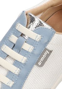 Zapatilla deportiva blanca de malla con acentos en azul, con detalles metálicos en plata, interior beige y cordones blancos. Etiqueta de marca visible en el lado.