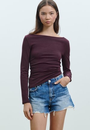 Top a maniche lunghe bordeaux con scollatura a barchetta e texture arricciata, abbinato a pantaloncini in denim chiaro con orli sfrangiati e vestibilità casual.