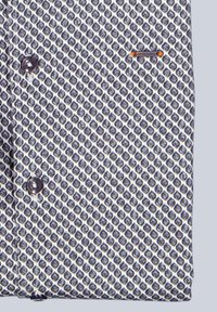 Weißes Hemd mit blauen Rautenmuster. Mit dunklen Knöpfen und einem kleinen Logo-Akzent in der Nähe der Brust. Glatter Stofftextur.