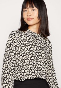 Blusa preta com padrão floral branco, design com colarinho, abertura frontal com botões, mangas longas e um corte ligeiramente solto.