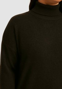 Sort turtleneck sweater lavet af blødt strikmateriale. Har en høj hals, afslappet pasform og ribbet tekstur ved kraven.
