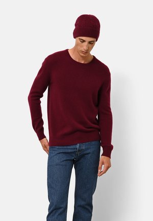 Pull en tricot bordeaux avec un col rond et des poignets côtelés, associé à un bonnet côtelé assorti, porté avec un jean en denim bleu.