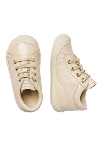 Sneaker in finta pelle beige con occhielli in metallo dorato, design con lacci, lati testurizzati e suola in gomma. Forma bassa e arrotondata.