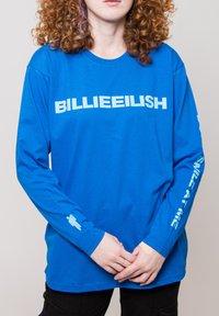 Blue long-sleeve t-shirt with “BILLIEEILISH” text in white across the front and graphic accents on the sleeves. Smooth cotton texture.