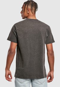 Tricou din bumbac gri închis, cu mâneci scurte și guler rotund, având un design simplu și o croială lejeră. Fără accente sau modele vizibile.