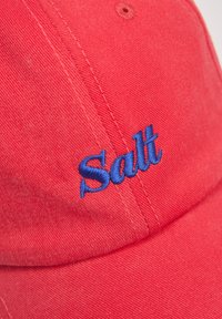 Czerwona bawełniana czapka baseballowa z niebieskim haftowanym napisem "Salt". Projekt zawiera przeszyte szwy i wygięty daszek.