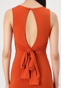 Robe couleur rouille avec un décolleté rond, dos nu et un lien à nouer à la taille, en tissu lisse et avec une fermeture à boutons.