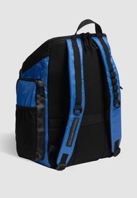 Mochila de nylon azul con respaldo de malla negra, correas de hombro acolchadas duales, bolsillo frontal con cremallera y material texturizado para ventilación.