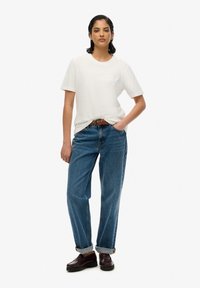 Witte katoenen t-shirt, relaxte pasvorm, gecombineerd met losse, rechte spijkerbroek in het blauw. Een bruine gevlochten riem en donkerbruine schoenen maken de look compleet.