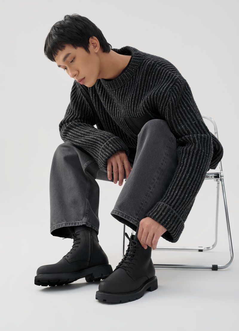 Schwarze Schnürstiefel mit knöchelhohem Design und strukturierten Gummisohlen, kombiniert mit grauen weiten Jeans und einem grob gestrickten schwarzen Pullover.