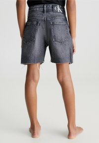 Pantalones cortos de mezclilla en negro desgastado, con una cintura alta, dobladillo deshilachado, dos bolsillos traseros y una etiqueta de marca en la cintura.
