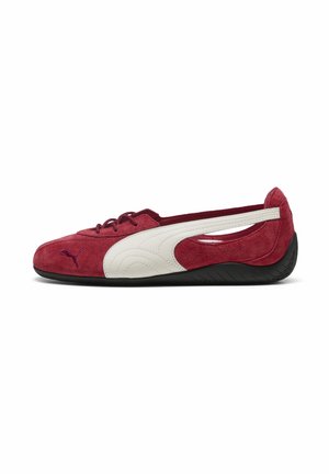 Chaussure Puma en daim rouge profil bas avec bande latérale blanche, semelle noire, fermeture à lacets à l'avant et design découpé au talon.