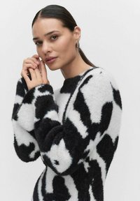 Mustavalkoinen abstrakti kuvioitu neulepaita, joka on valmistettu pehmeästä, teksturoidusta materiaalista, leveillä hihoilla ja rennolla istuvuudella.