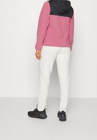 Giacca in fleece rosa con pannello superiore nero, abbinata a joggers grigi chiari e scarpe da ginnastica nere. Design semplice, texture morbida.