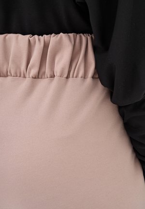Szczegół elastycznego pasa w jasno różowych spodniach z wysokim stanem, zestawionych z czarną, luźną bluzką.