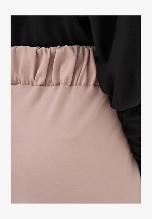 Szczegół elastycznego pasa w jasno różowych spodniach z wysokim stanem, zestawionych z czarną, luźną bluzką.