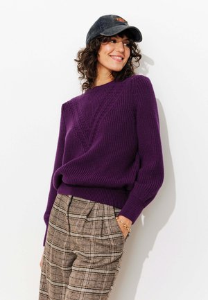 Pull en maille violet avec un motif en losanges texturé, col rond et poignets côtelés. Associé à un pantalon à carreaux dans des tons terre.