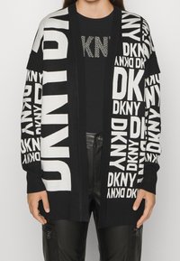 Svart och vit stickad cardigan med iögonfallande "DKNY" logotryck, öppen framsida och ribbade manschetter. Matchas med en svart t-shirt och läderbyxor.