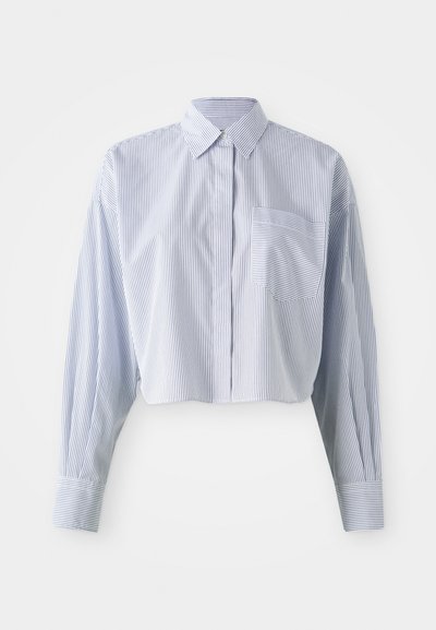 Chemise cropped en rayures verticales bleu et blanc, avec un col pointu, des manches longues et une poche avant. Texture en coton lisse.