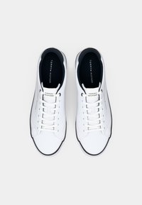 Paire de baskets basses blanches Tommy Hilfiger avec lacets blancs et doublure intérieure noire, vue de dessus sur un fond uni.