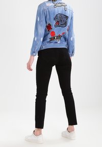 Ljusblå denimjacka med broderade lappar inklusive en panter och rosor; ihopsatt med svarta tajta byxor och vita sneakers.