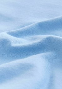 Tissu en coton bleu clair avec une texture lisse, montrant de douces plis et rides, démontrant un tissage doux et uniforme ainsi que des détails de surface.