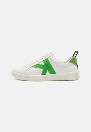 White sneakers featuring a green fabric accent and logo, textured sole with vertical grooves, rounded toe, and flat laces.