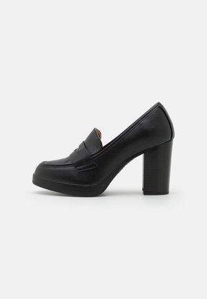 Mocassins noirs à talons hauts avec un bout arrondi, en simili cuir, avec une sangle avant et un talon bloc texturé.