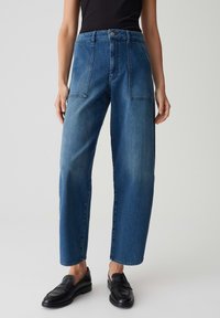 Hoge taille blauwe denim jeans met wijde pijpen, voorzien van twee voorzakken en subtiele vervaging, gecombineerd met zwarte instappers.
