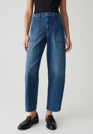 Hochtaillierte blaue Denim-Jeans mit weitem Bein, ausgestattet mit zwei vorderen Taschen und dezenten Verwaschungen, kombiniert mit schwarzen Slippern.