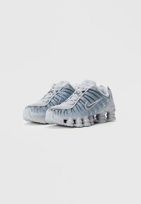 Αθλητικά παπούτσια ανοιχτού γκρι χρώματος με ημιδιαφανές μπλε μέσο από πλέγμα, παχύ, μαλακό πέλμα και έντονα αυλάκια στα πλάγια. Παρουσιάζουν ασημένιες λεπτομέρειες.