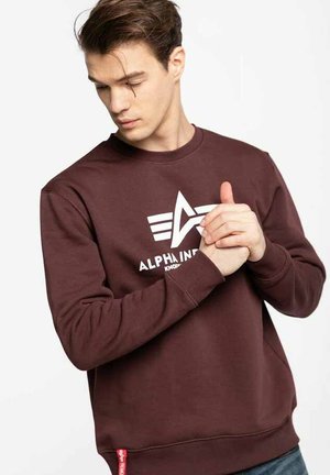 Maroon sweatshirt made of cotton blend, featuring a white logo and star design. Crew neck and ribbed cuffs. Side tag with text detail.
