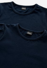 Meresinist sinistest puuvillast T-särgid kuhjatud, millel on ümardatud kaelused ja pehmed tekstuurid, mõlemal särgil "NEXT" sildid krae peal.