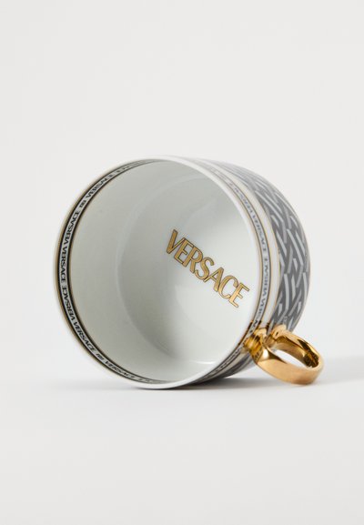 Biały porcelanowy kubek do kawy z geometrycznym szarym wzorem, złotym uchwytem i napisem "VERSACE" w złotych literach wewnątrz.