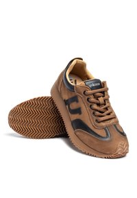 Baskets en daim marron avec accents noirs, bout arrondi, laçage à l'avant et semelle en caoutchouc texturée avec un motif en zigzag.