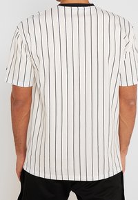 Camiseta blanca de manga corta con rayas verticales negras, escote redondo y corte relajado. Material de algodón suave con textura lisa.
