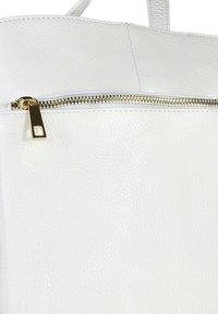 Witte, gestructureerde leren tas met een gouden rits en bijpassende trekknop op de voorklep, waarbij de bovenrand en handgreep zichtbaar zijn.