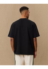 T-shirt preta de manga curta com um corte descontraído, apresentando um decote redondo e uma textura suave. Apresentada de costas contra um fundo neutro.