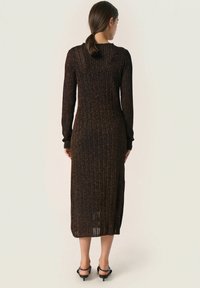 Robe longue ajustée en tissu tricoté sombre avec des côtes verticales et des accents métalliques. Dotée de manches longues et d'une longueur mi-mollet.