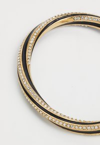 Goldfarbener Armreif mit Akzenten aus schwarzem Emaille, der eine Reihe von klaren Strasssteinen entlang der Oberfläche und ein glattes, gebogenes Design aufweist.